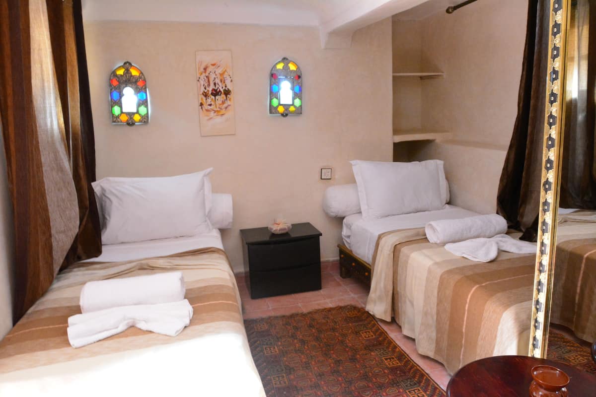 A hotel room with two beds, a small black nightstand, a mirror, and two stained glass windows.