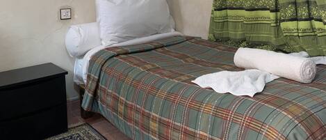 A bedroom with a bed, a nightstand, a patterned rug, a decorative mirror, and a green curtain.