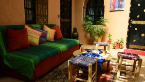 A cozy living room with a green sofa, colorful cushions, a patterned rug, and wooden chairs. - Auberge Ayam Atlas (Ourika)