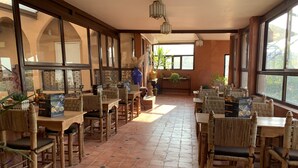 A spacious dining area with wooden tables and chairs, large windows, and potted plants. - Auberge Ayam Atlas (Ourika)
