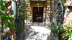 A narrow pathway leading to a building entrance with a wrought iron gate, surrounded by potted plants and a lattice structure. - Auberge Ayam Atlas (Ourika)