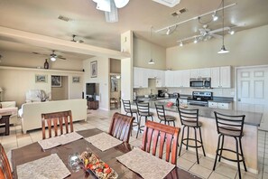 A spacious kitchen with white cabinets, a central island with bar stools, and a dining area with wooden chairs and placemats.