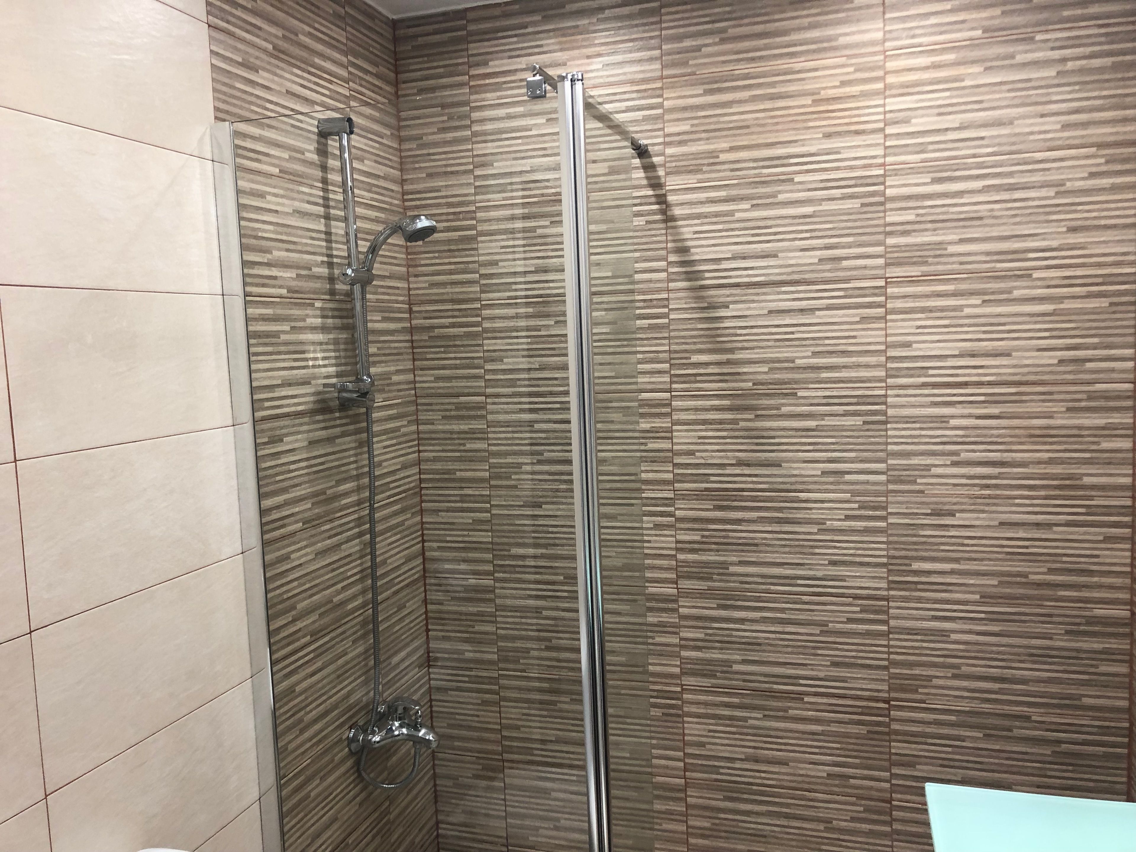 A shower with a glass door and a wooden wall pattern.
