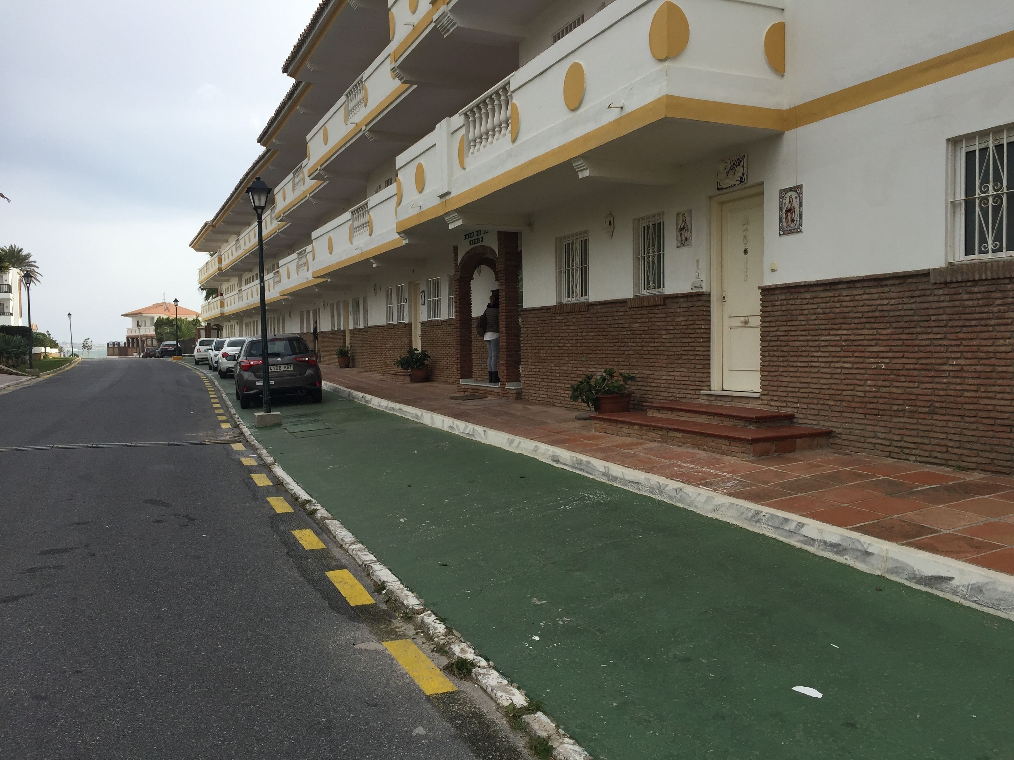 Un hotel a più piani con una pista ciclabile verde, auto parcheggiate e una facciata in mattoni.