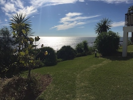 Un espace verdoyant avec vue sur la mer, entouré de palmiers et bordé d’une structure blanche.