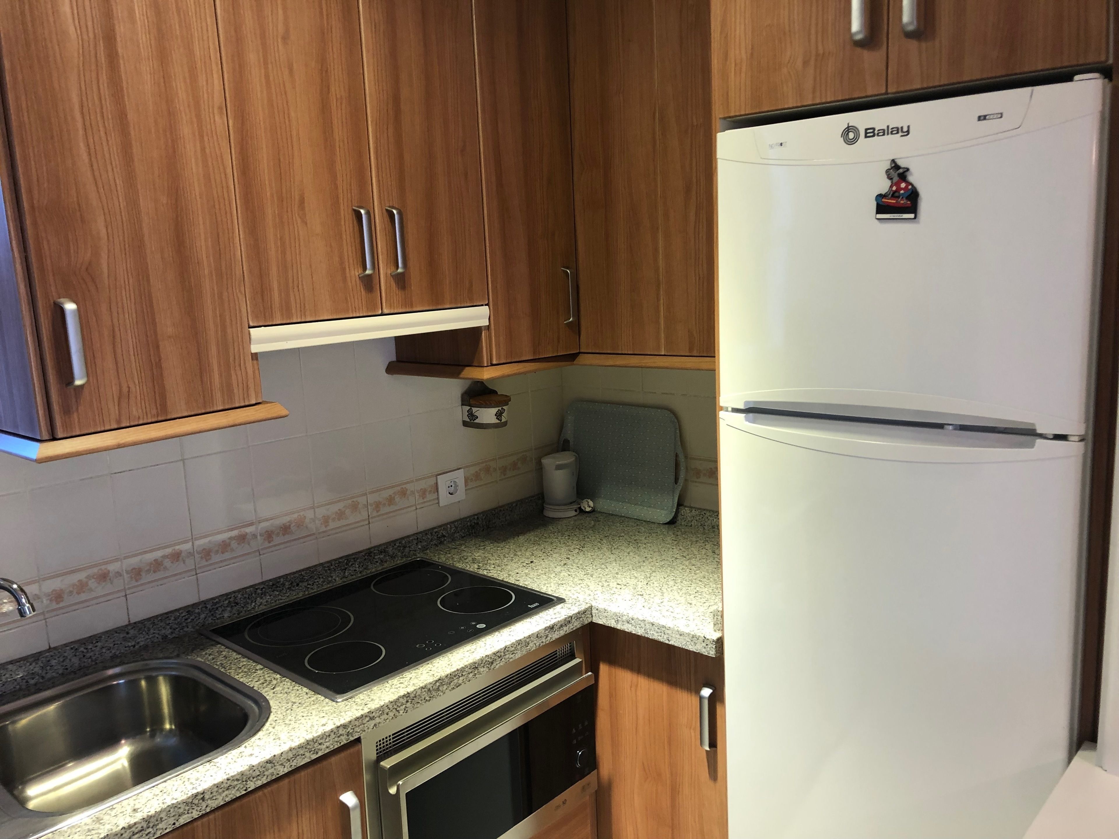 Uma cozinha compacta com armários de madeira, uma geladeira Balay, forno embutido, micro-ondas e pia.