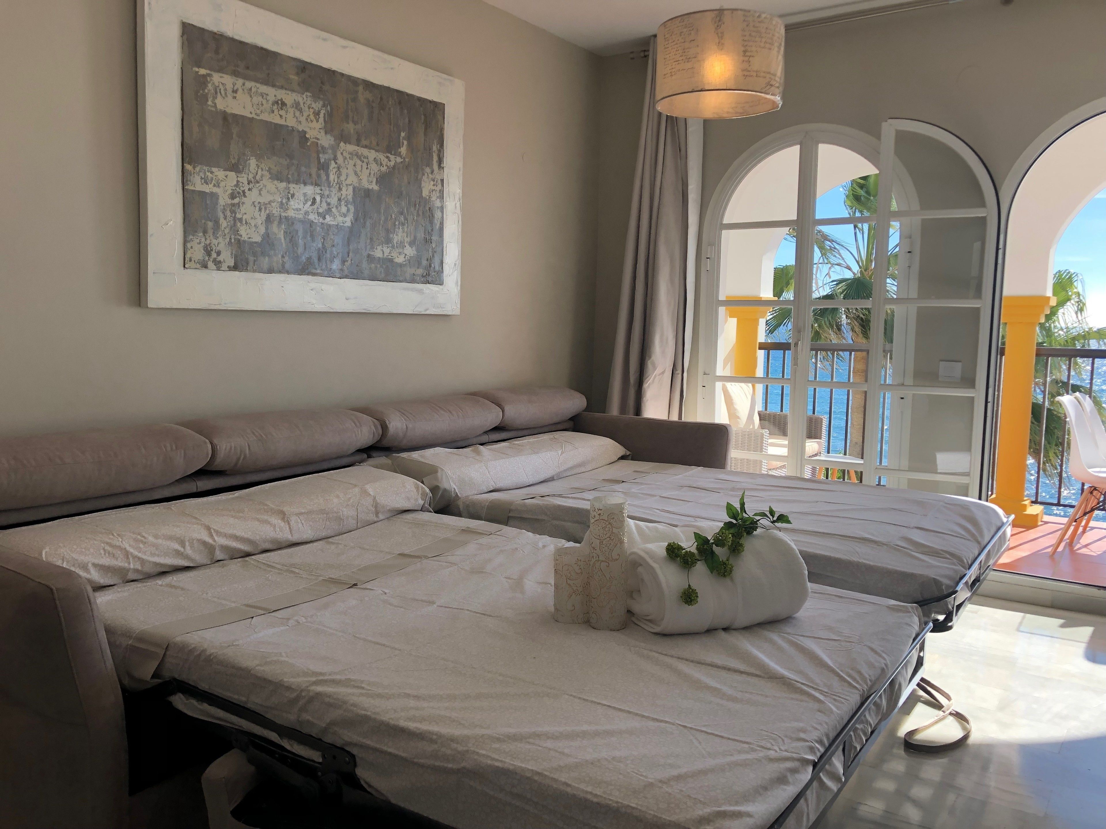 A hotel room with a large bed, a view of the sea through a balcony, and a painting on the wall.