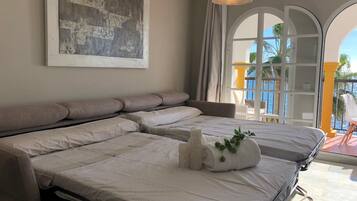 A hotel room with a large bed, a view of the sea through a balcony, and a painting on the wall.