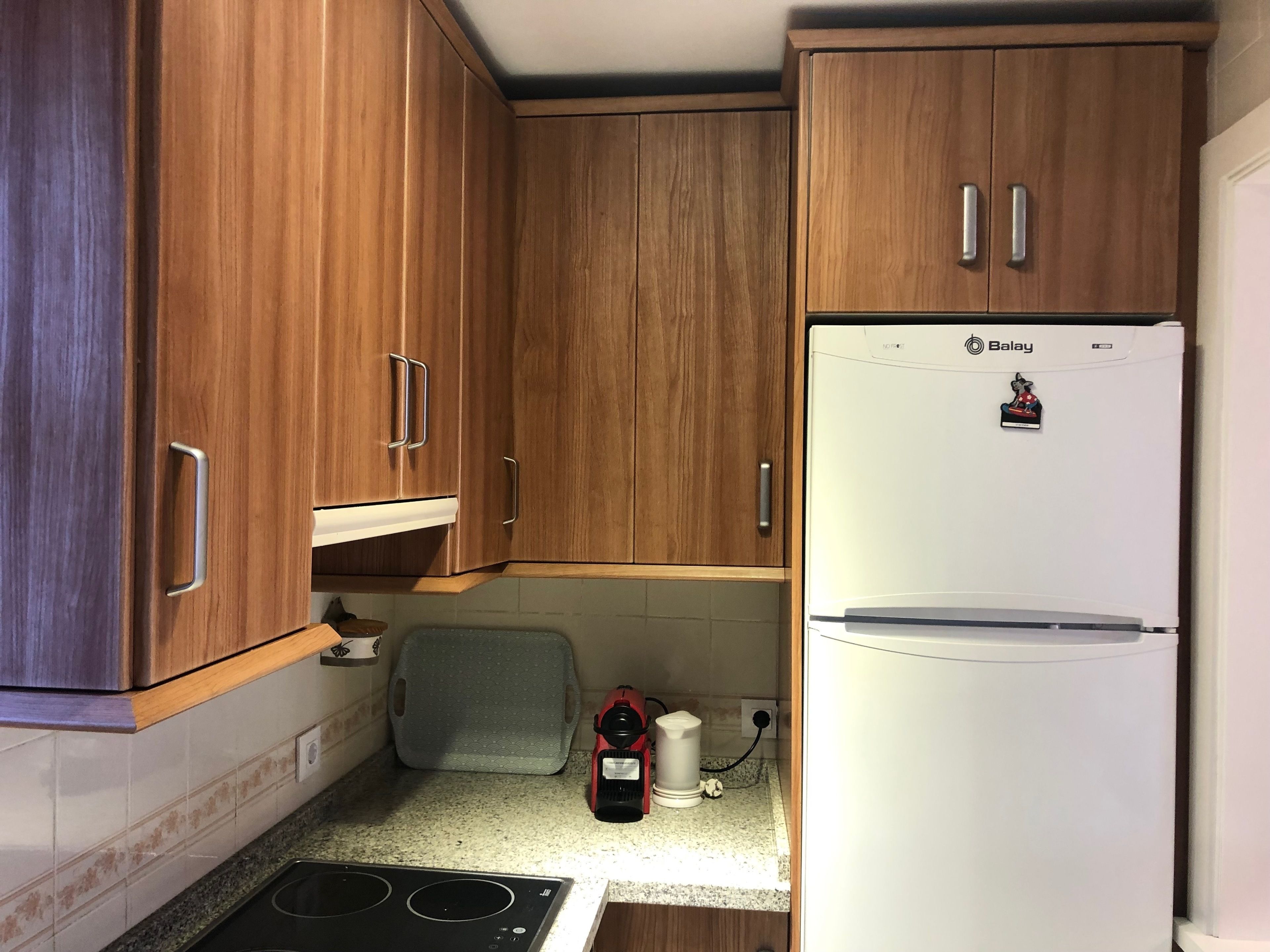 A compact kitchen with wooden cabinets, a white refrigerator, a gas stove, and a kettle on the countertop.