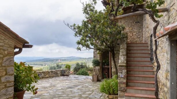 A stone courtyard with a staircase leading to a wooden door, surrounded by potted plants and a view of distant hills. - The Porchereccia delle Bartaline (Panzano in Chianti)