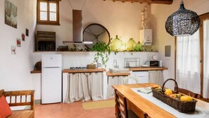 A cozy kitchen with a wooden table, a refrigerator, a sink, and a hanging light fixture. - The Porchereccia delle Bartaline (Panzano in Chianti)