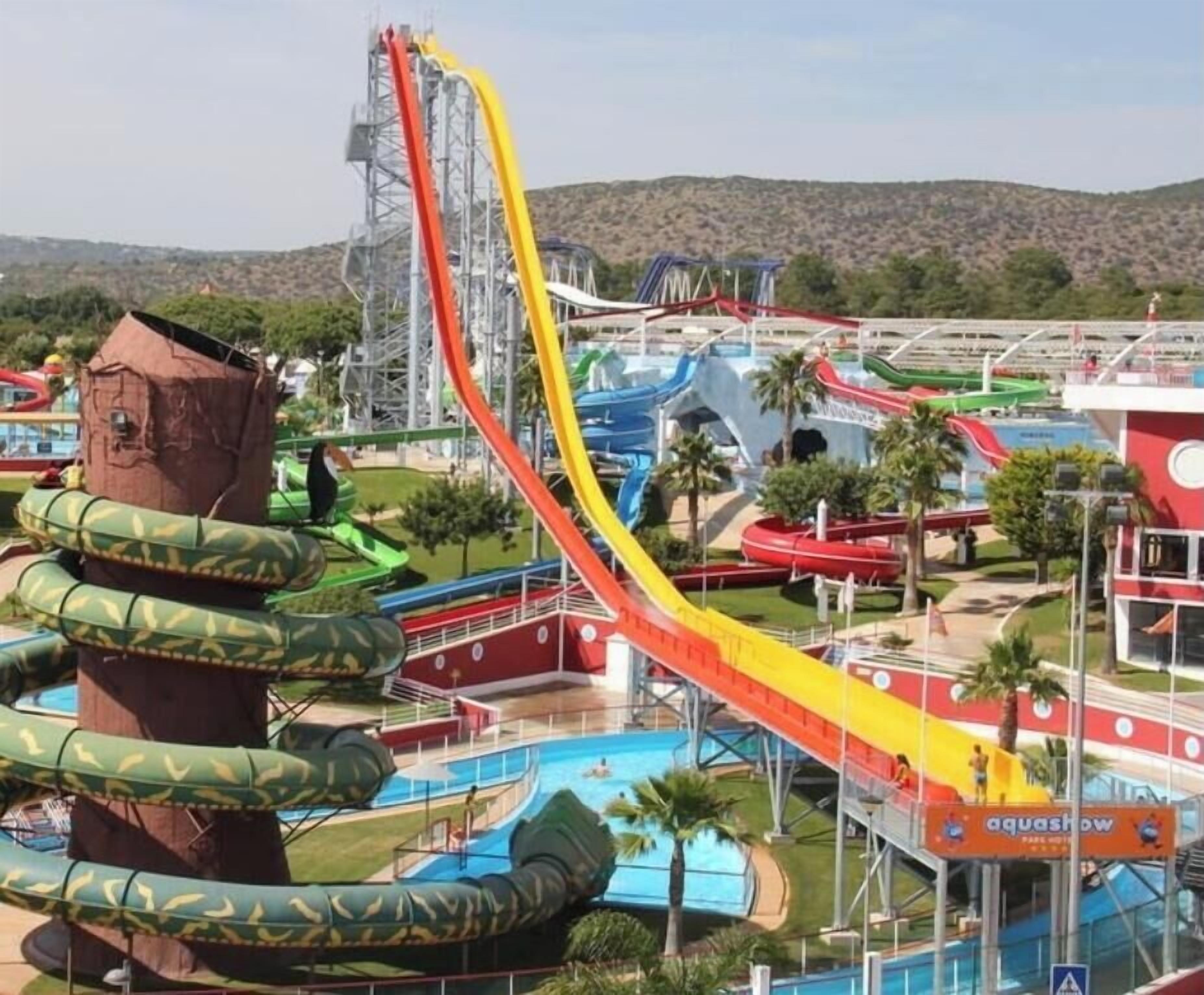 An amusement park with a large roller coaster, a water slide, and a pool area.