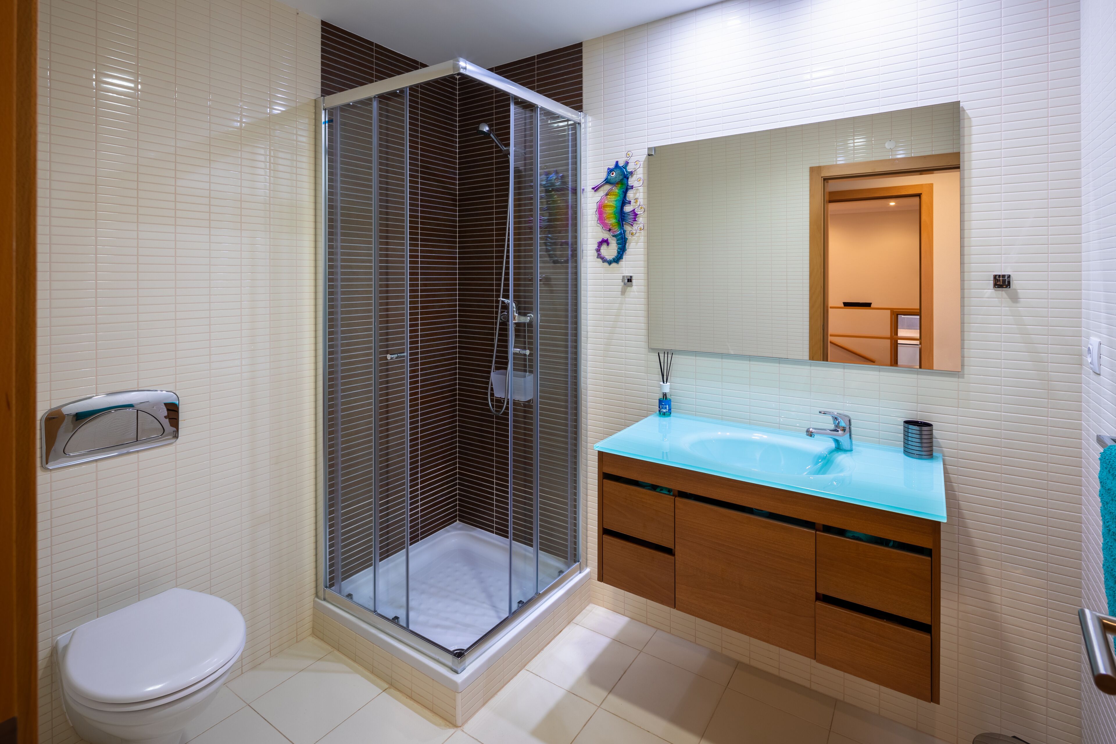 Une salle de bain moderne avec une douche à parois de verre, des toilettes blanches et un meuble-lavabo doté d’un plan de travail bleu.