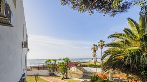 A coastal property with a paved pathway leading to a beach, palm trees, and a white building with a window and air conditioning unit. - Cubo's Apartamento Doña Lola / communal swimming pool / free wifi / near beach (La Cala de Mijas)