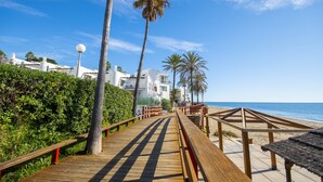 A wooden boardwalk leading to a beach with palm trees and a clear blue sky. - Cubo's Apartamento Doña Lola / communal swimming pool / free wifi / near beach (La Cala de Mijas)
