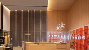Un moderno área de recepción de hotel con un mostrador de madera, un ventanal con persianas y un letrero de neón que dice "ATWELL SUITES".