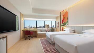 Habitación de hotel con vista a la ciudad, un escritorio, dos camas y un televisor.