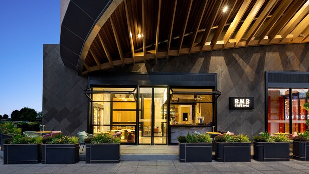 Un edificio moderno con fachada curva, amplios ventanales de vidrio y área de estar exterior con macetas.