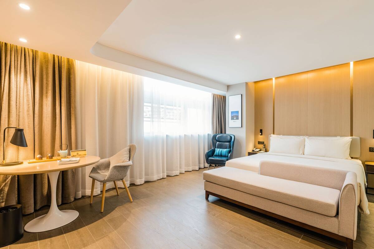 A hotel room with a bed, a desk, a chair, and a window with curtains.