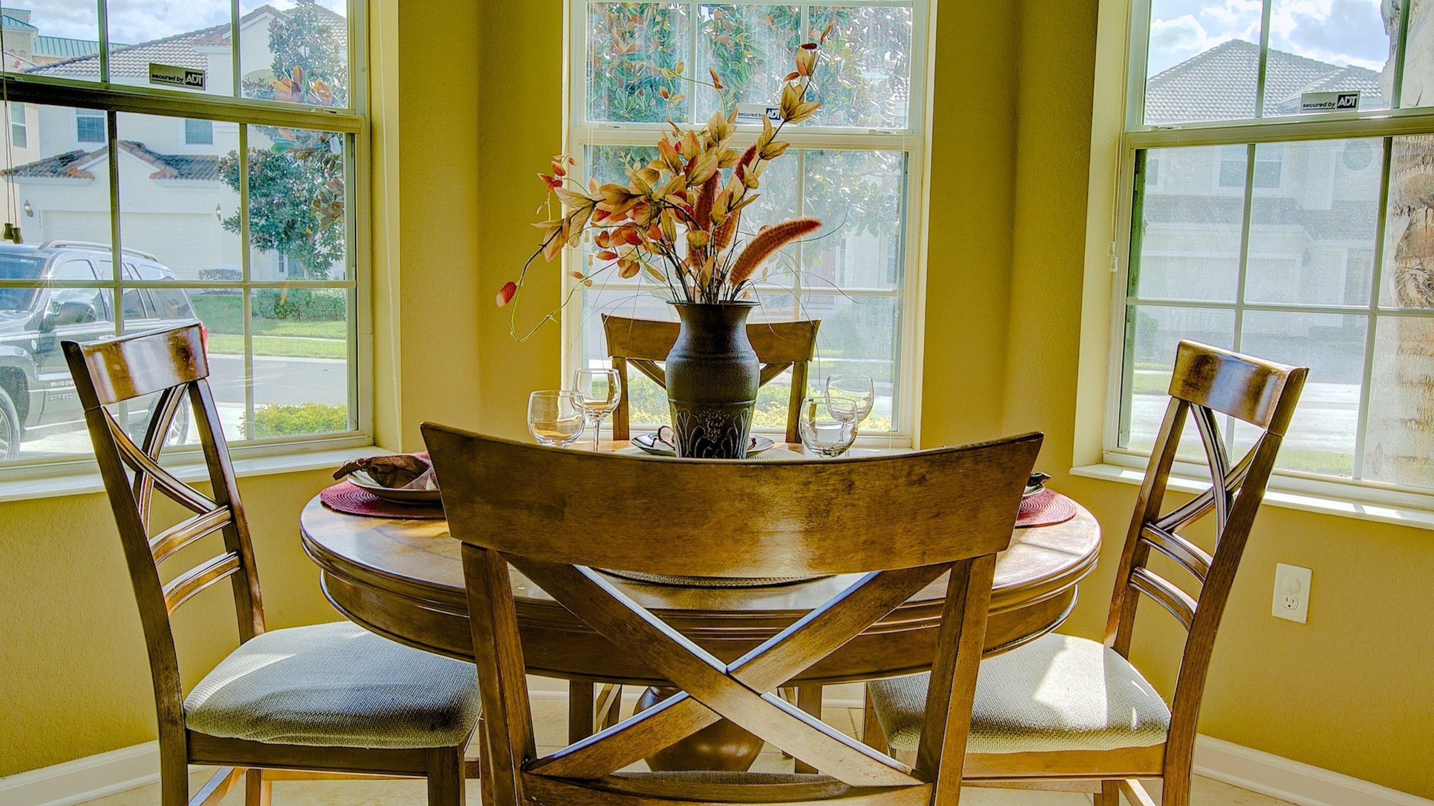 Un coin repas avec une table ronde, quatre chaises en bois et un vase rempli de fleurs.