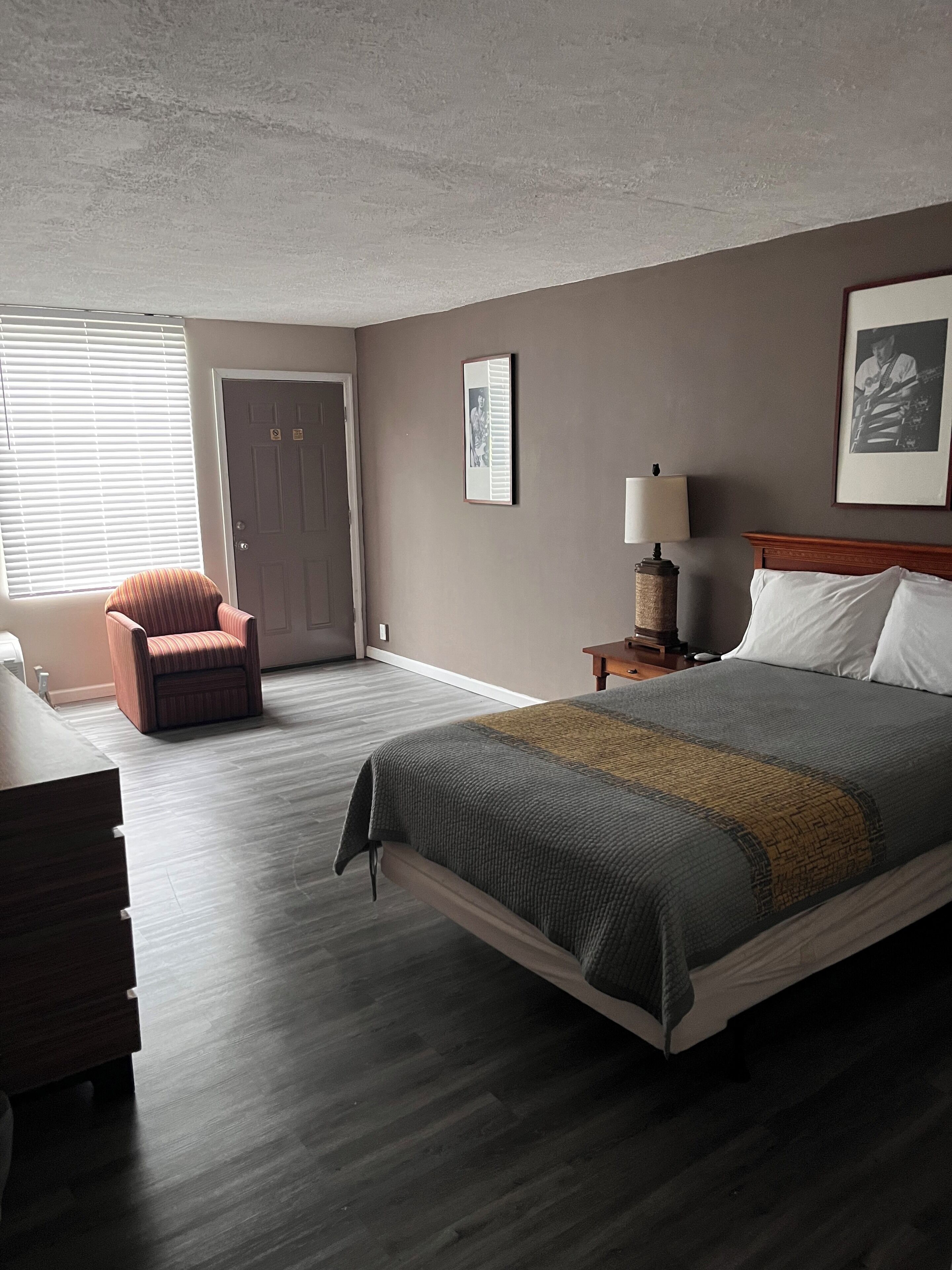 Une chambre à coucher avec un lit, une chaise, une table de chevet, une lampe et une porte.