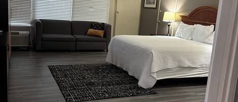 A bedroom with a bed, a sofa, a rug, and a door.