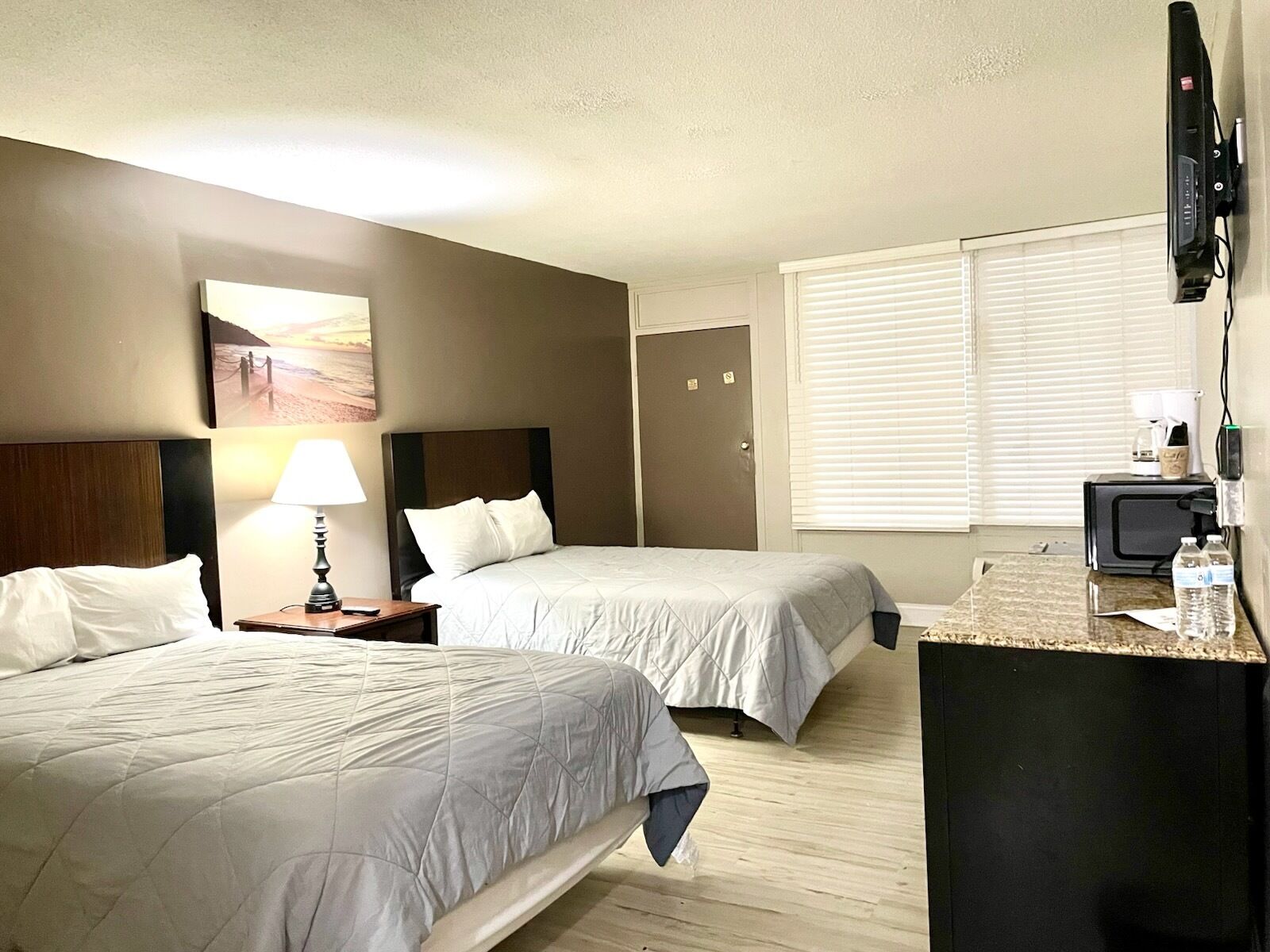 Une chambre d’hôtel avec deux lits, un bureau, une télévision et une fenêtre avec des stores.