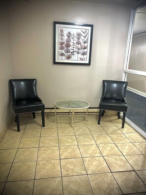 Quarto com duas cadeiras de couro preto, uma mesa redonda de vidro e uma impressão botânica emoldurada na parede.