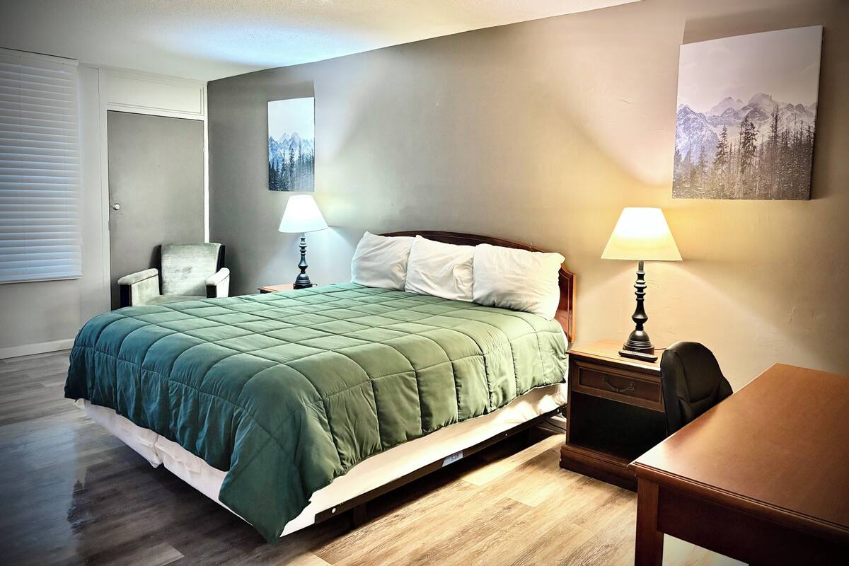 Un dormitorio ordenado con cama, dos mesitas de noche, una silla, un escritorio y dos lámparas de pared.