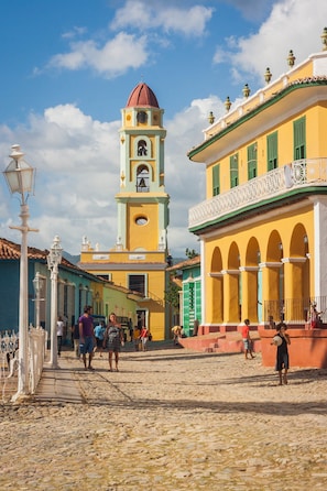 Una plaza histórica con adoquines, una imponente torre del reloj y edificios coloridos con balcones.