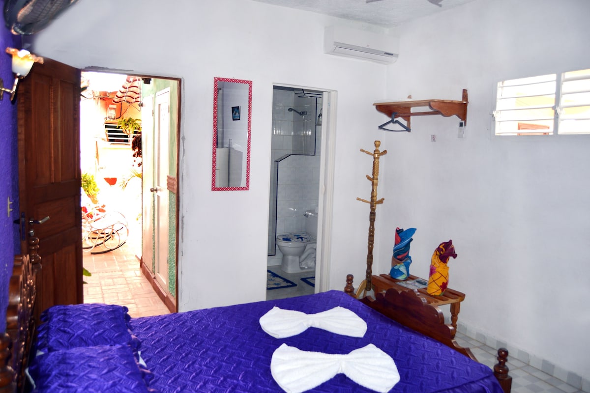 Una habitación con cama, una silla de madera, un espejo y una ventana.