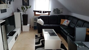 Ein modernes Wohnzimmer mit einer schwarzen Ledersofa, einem weißen Couchtisch, einem Flachbildfernseher und einem Bücherregal.