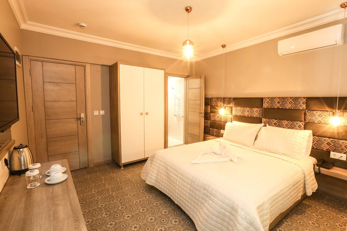 Quarto de hotel com cama, guarda-roupa, mesa de cabeceira com chaleira e chão estampado.