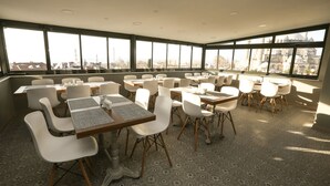 Amplia habitación con ventanas grandes, sillas blancas y mesas dispuestas para comer.