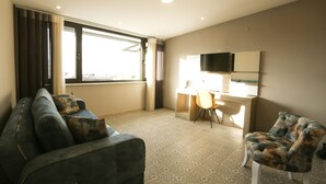 Habitación de hotel con sofá, sillón, escritorio y televisor.