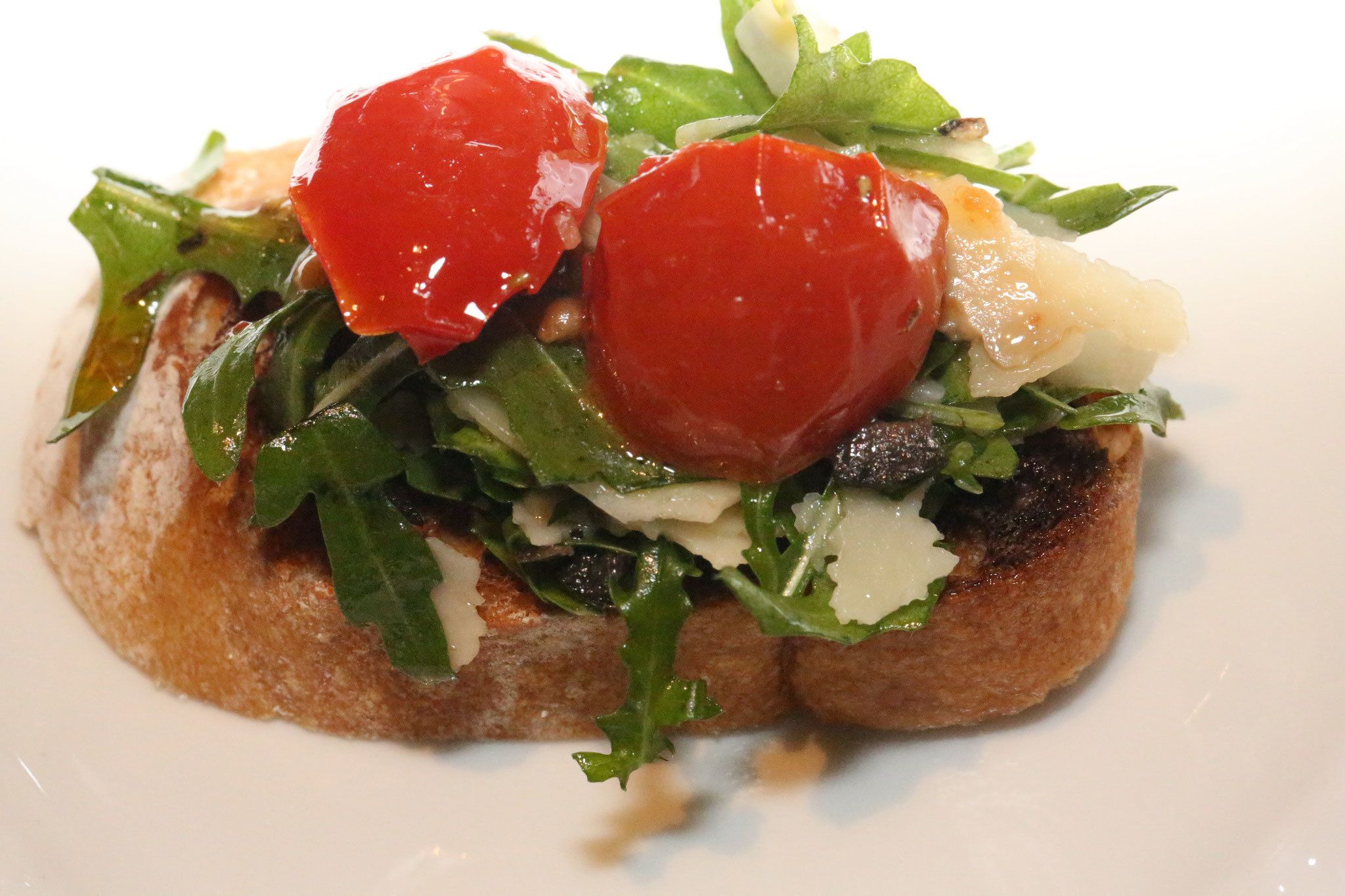 Sanduíche com tomate, folhas verdes e queijo sobre uma fatia de pão.
