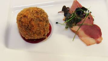 Ein weißer Teller mit einem runden, panierten Gericht und einer Fleischscheibe mit Salat.