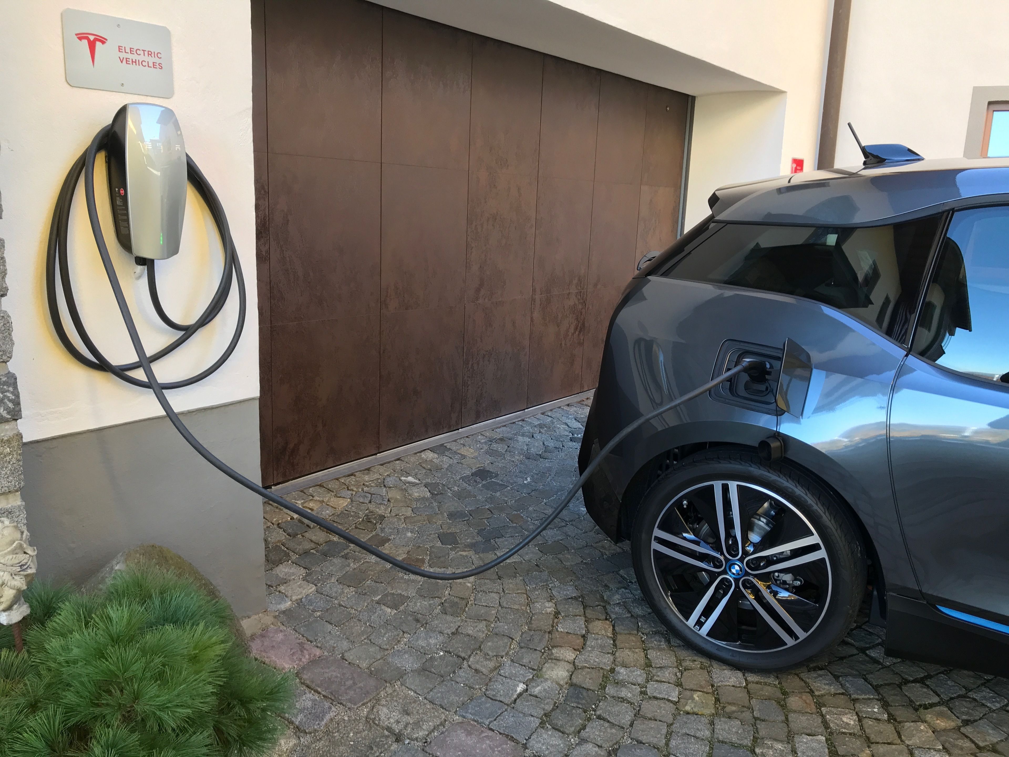Um veículo elétrico Tesla carregando em uma estação, com uma placa indicando ser para veículos elétricos.