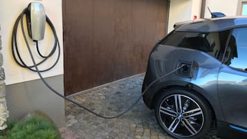 Um veículo elétrico Tesla carregando em uma estação, com uma placa indicando ser para veículos elétricos.