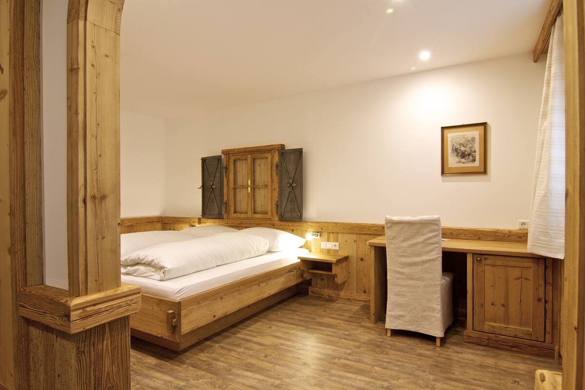 A wooden bedroom with a bed, nightstand, and a small desk with a chair.