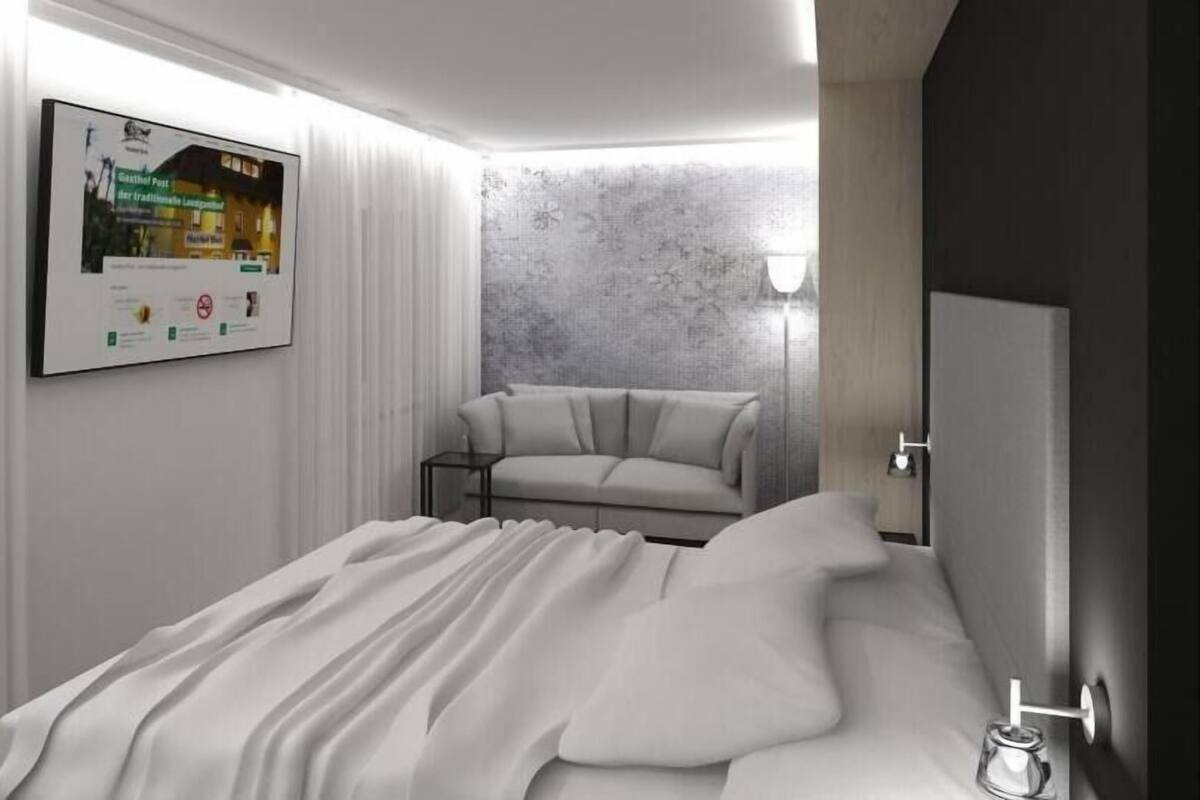 A modern bedroom with a bed, a sofa, a wall-mounted poster, and a textured wall.