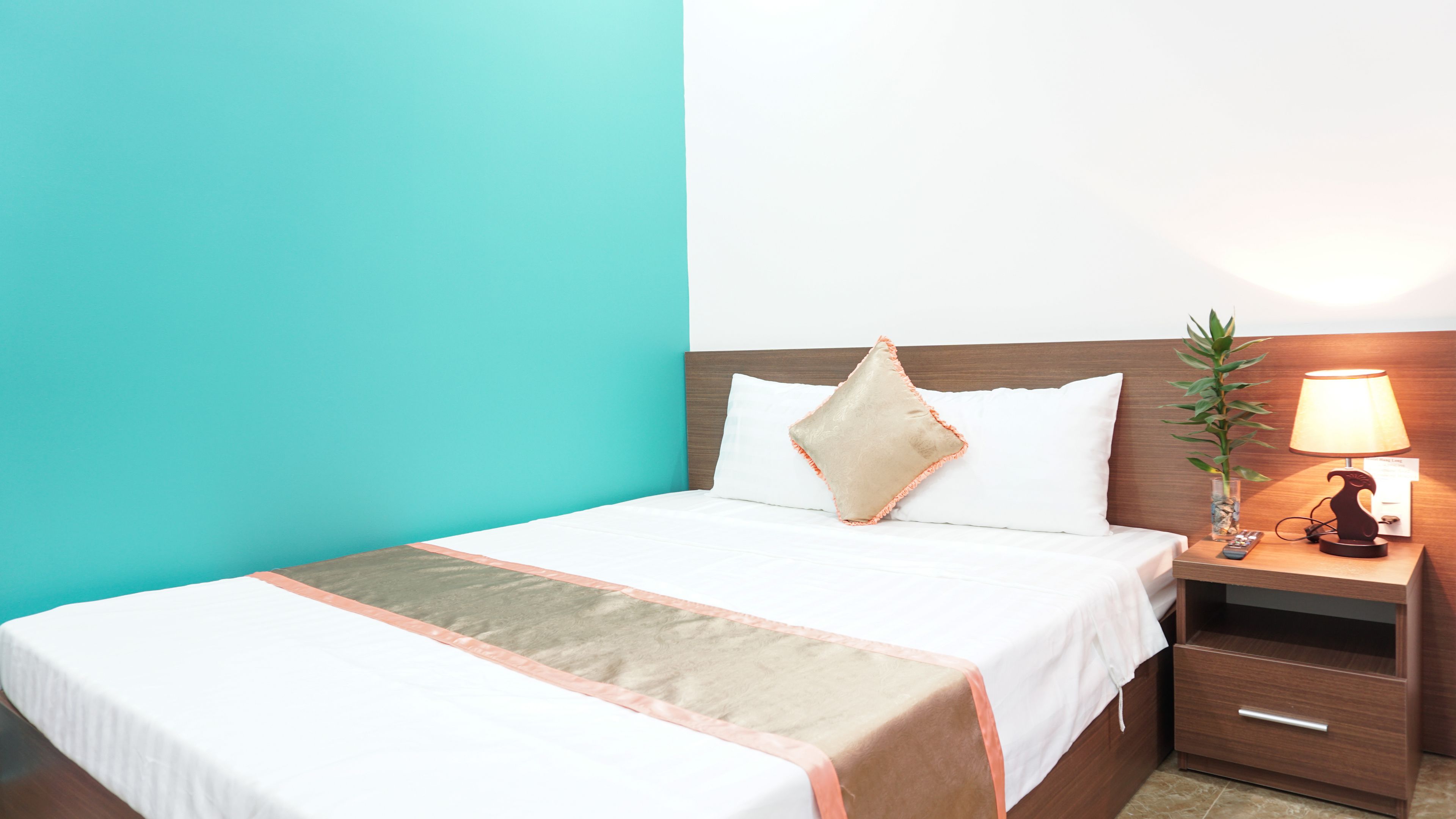 A hotel room with a bed, a nightstand, a lamp, and a plant.