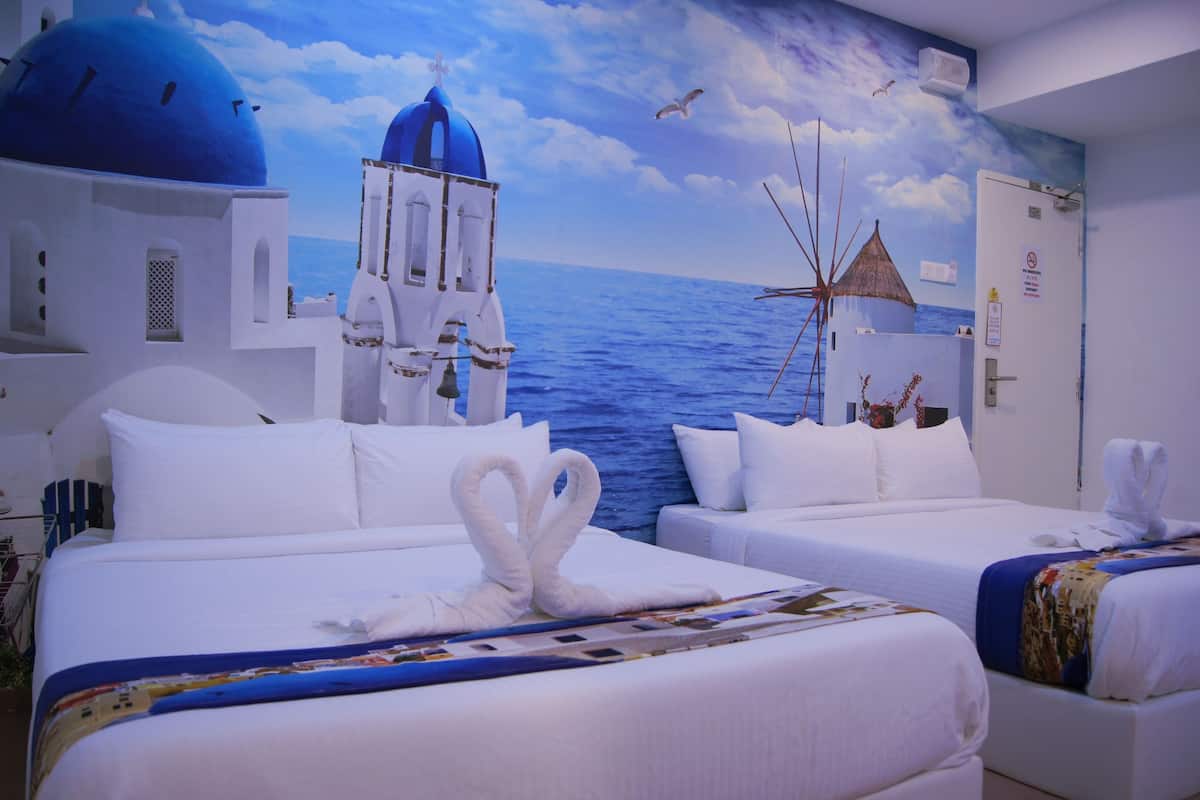 A hotel room with two beds, white bedding, and a mural of a blue sky, sea, and white buildings.
