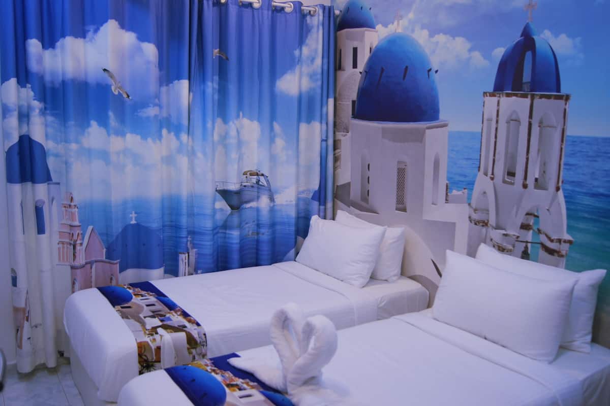 A hotel room with two beds, a view of the sea, and a mural of blue buildings and clouds.