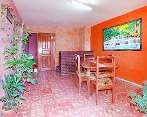 A dining area with a brick fireplace, wooden dining table and chairs, and a painting on the wall. - Caridad and Friends Rooms (Trinidad)
