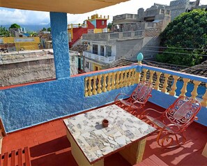 A balcony with a tiled table and two red chairs, overlooking a cityscape with colorful buildings. - Caridad and Friends Rooms (Trinidad)