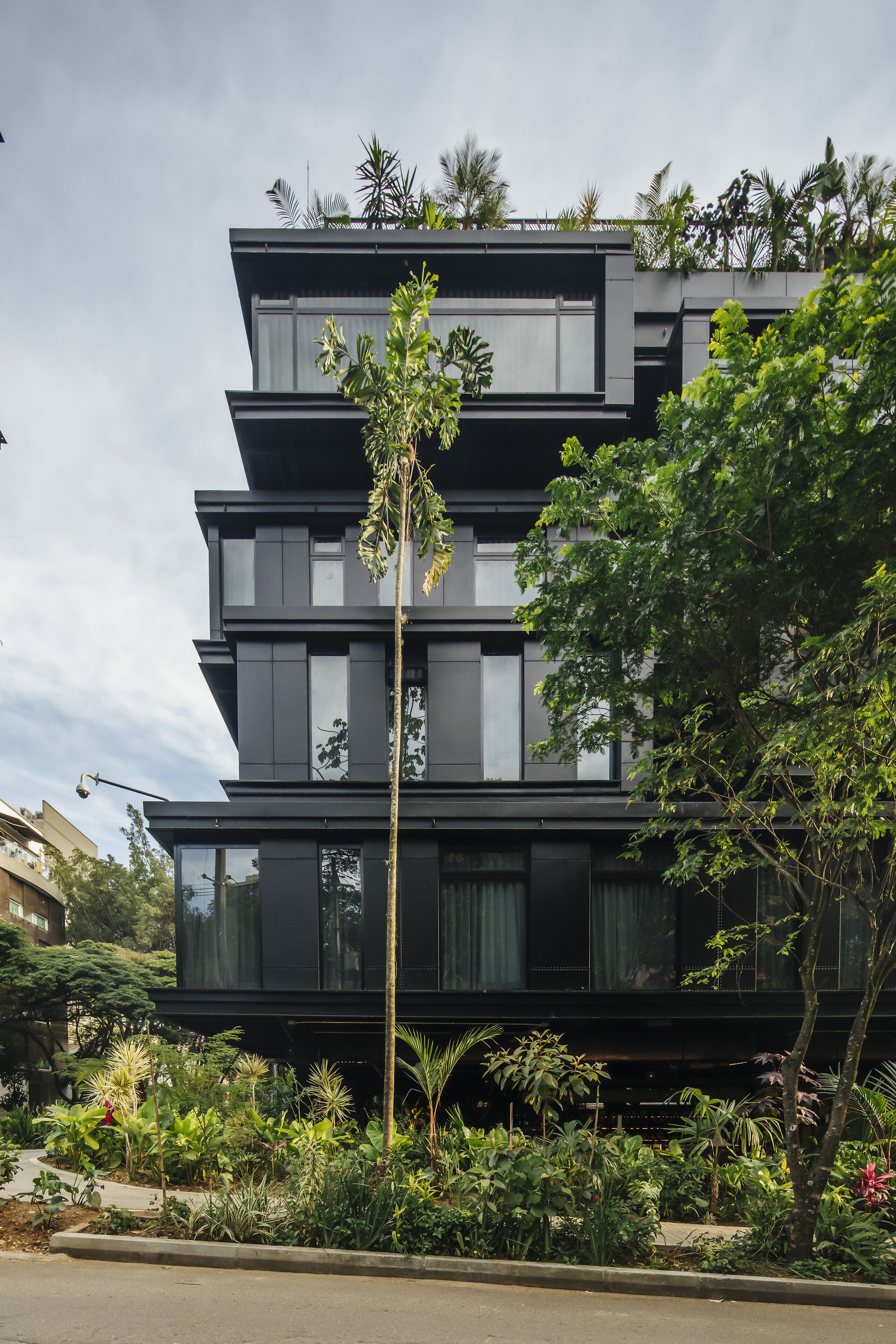 A modern multi-story building with a flat roof, surrounded by lush greenery and a well-maintained garden.
