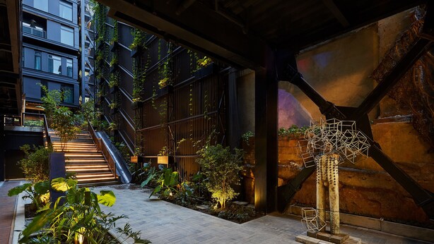 Un atrio interior con una escalera, plantas y una escultura metálica única.