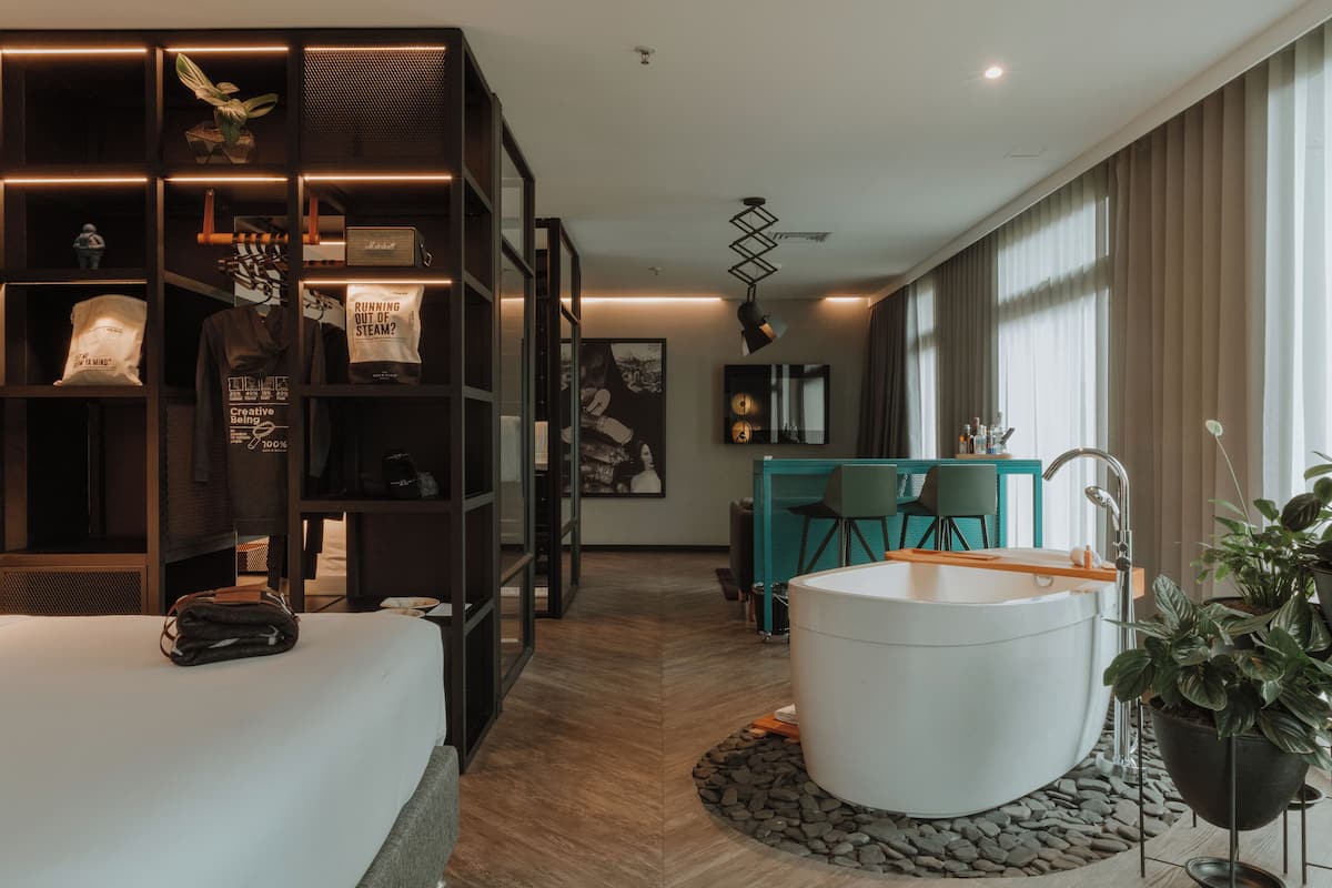 A modern hotel room with a large bed, a built-in wardrobe, a bathtub, and a dining area with a view.