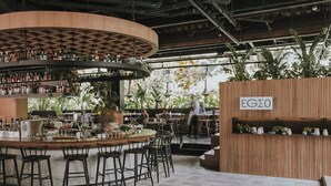 Zona de bar con mostrador circular, varios taburetes y estanterías llenas de botellas.